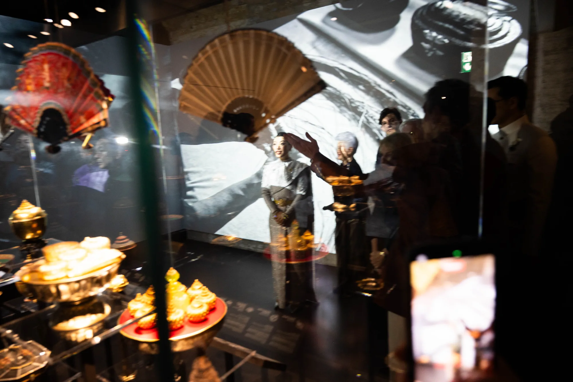 Layered exhibition scene with reflections and visitors, photographed by Helen Milova